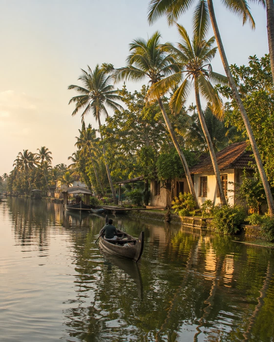 A traditional canoe on the Alleppey backwaters at golden hour, palm-lined banks and a Kerala house beside the water.